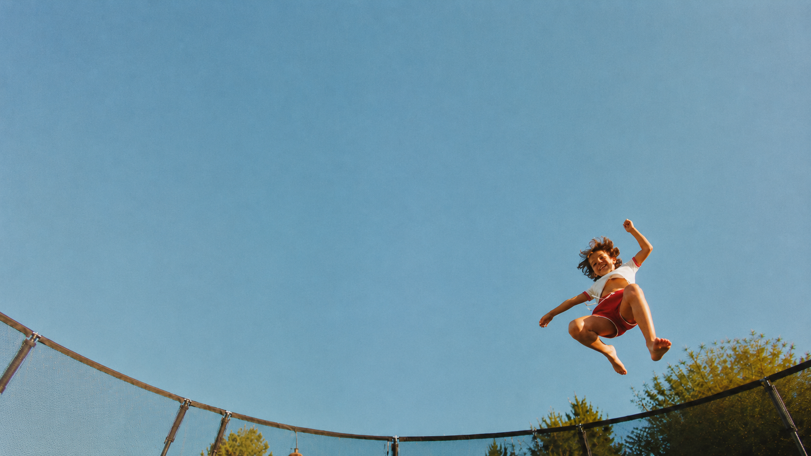 Child jumping on a trampoline against a blue sky
